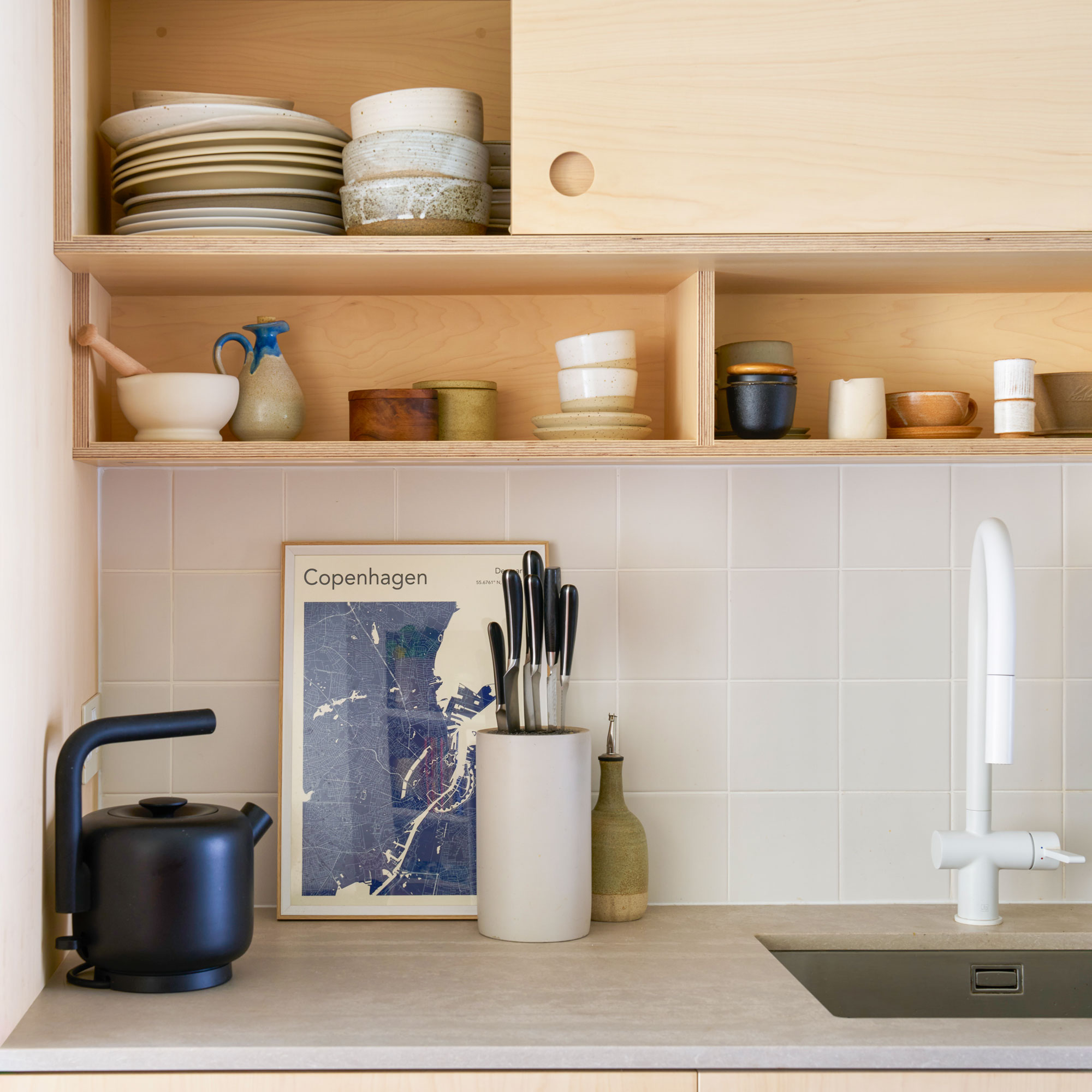 Plywood kitchen cabinets with white tiles, and a concrete look worktop with crockery on display