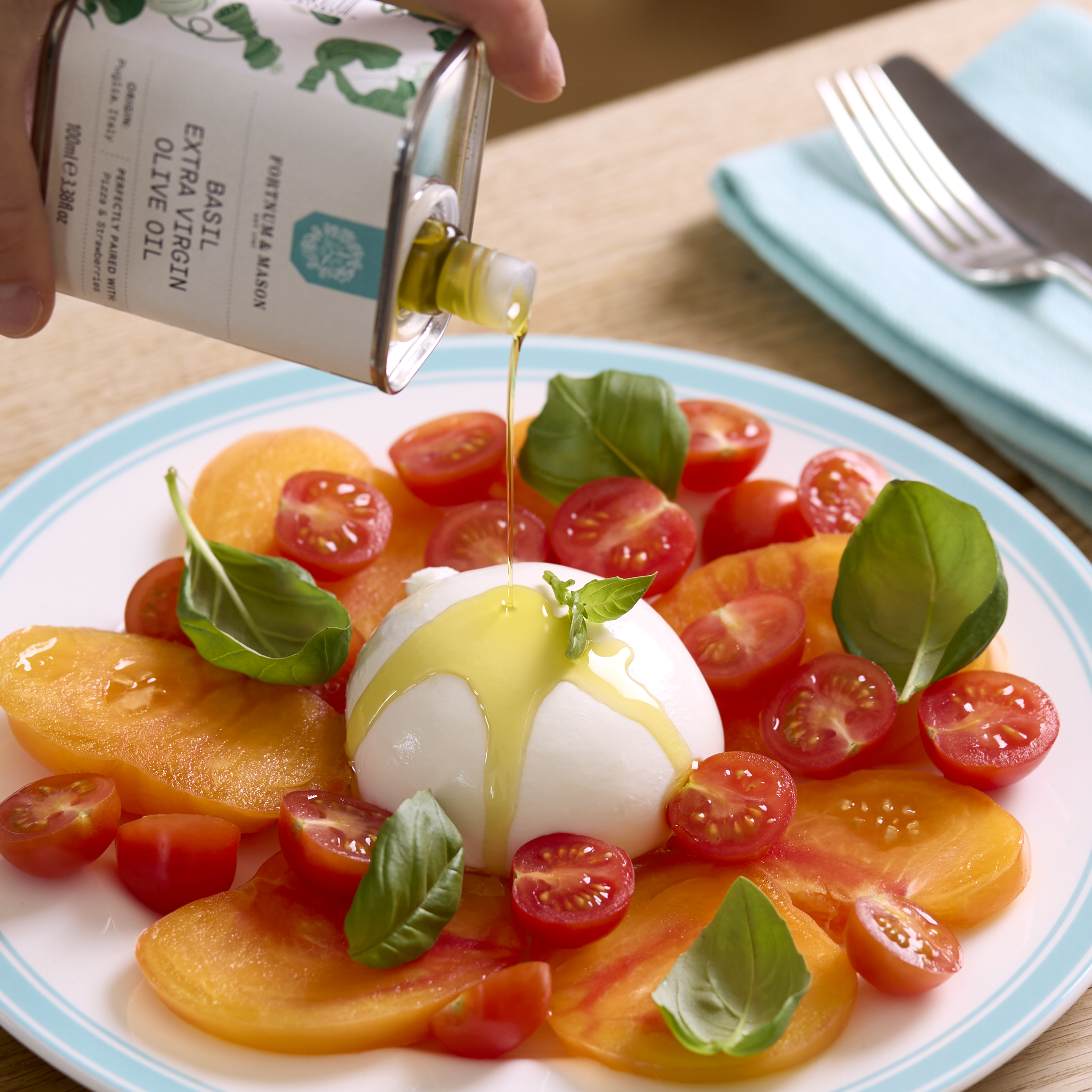 Basil-infused olive oil being poured onto burrata and tomatoes