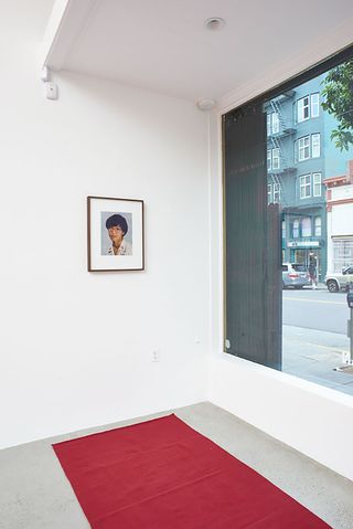 White wall with a portrait hanging and a red matt on the floor