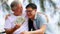 An older man embracing his young, smiling son and handing him a stack of cash