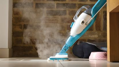 A blue and white Black & Decker steam mop being used on a tile floor. An exposed brick wall blurred out in the background