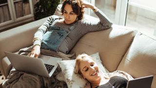Two women sitting on a couch using electronic devices