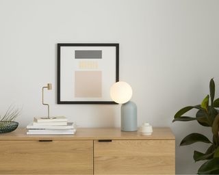 Vetro Table Lamp in blue on sideboard with plant, artwork and a stack of books