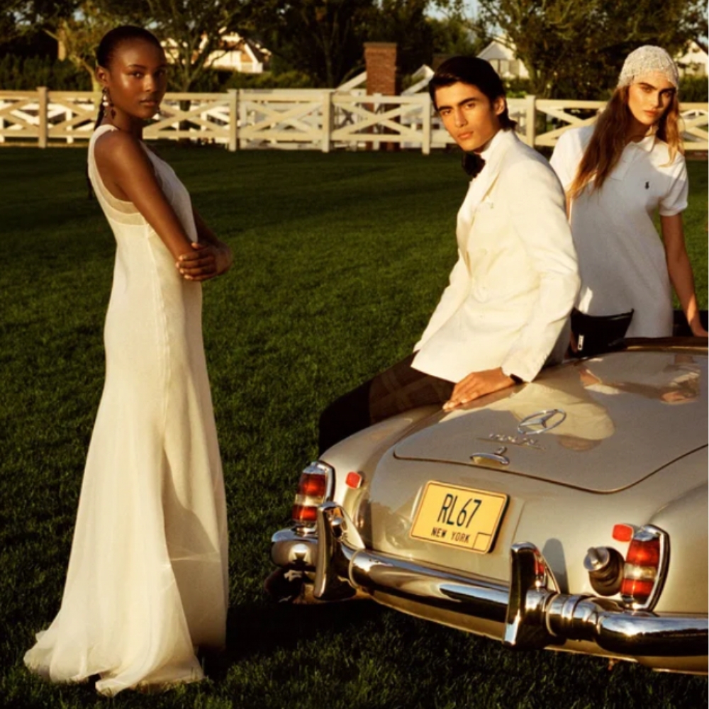 Two woman and a man standing near car, all dressed in white formal wear from FARFETCH