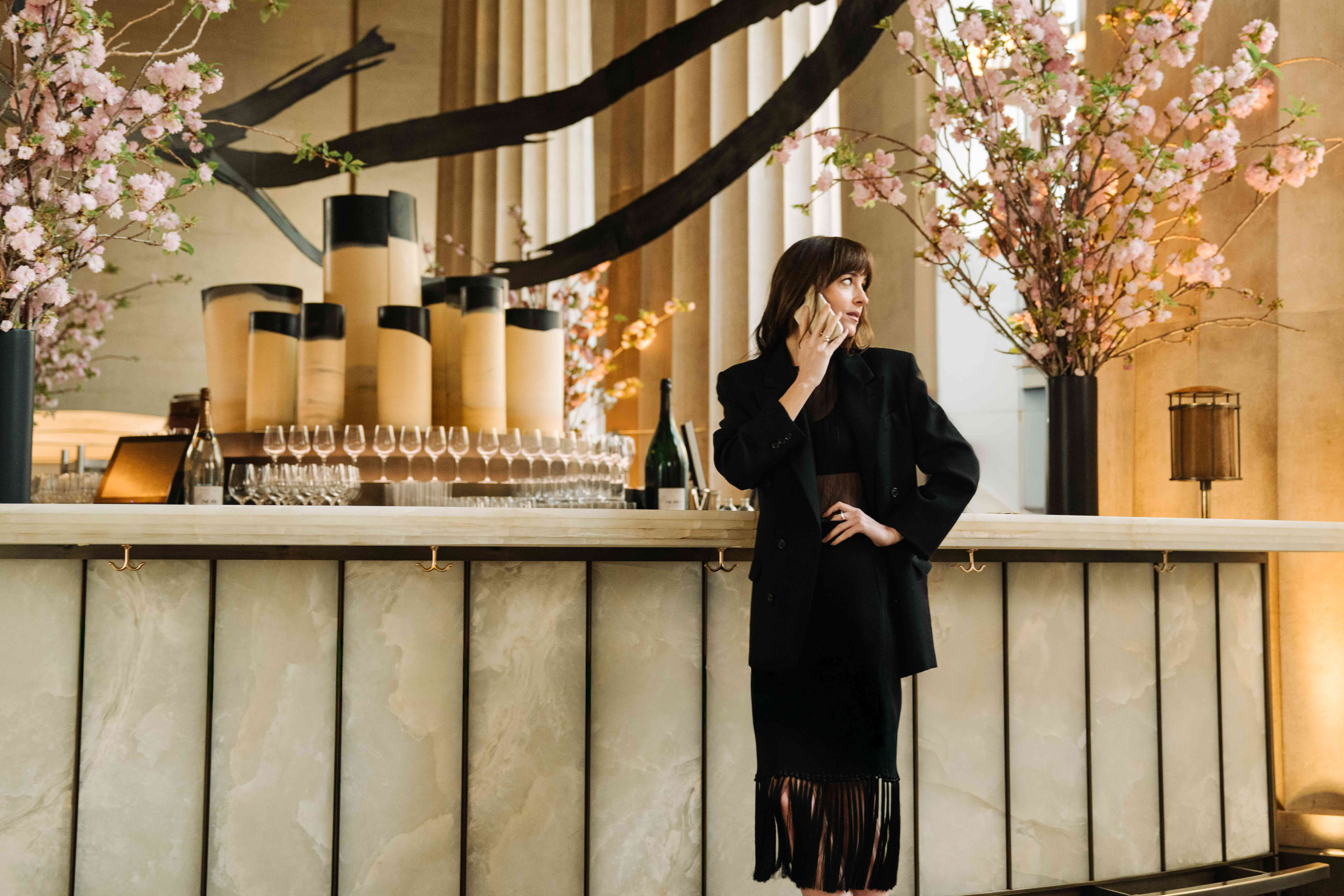 Dakota Johnson at a bar wearing a fringe dress and longline blazer