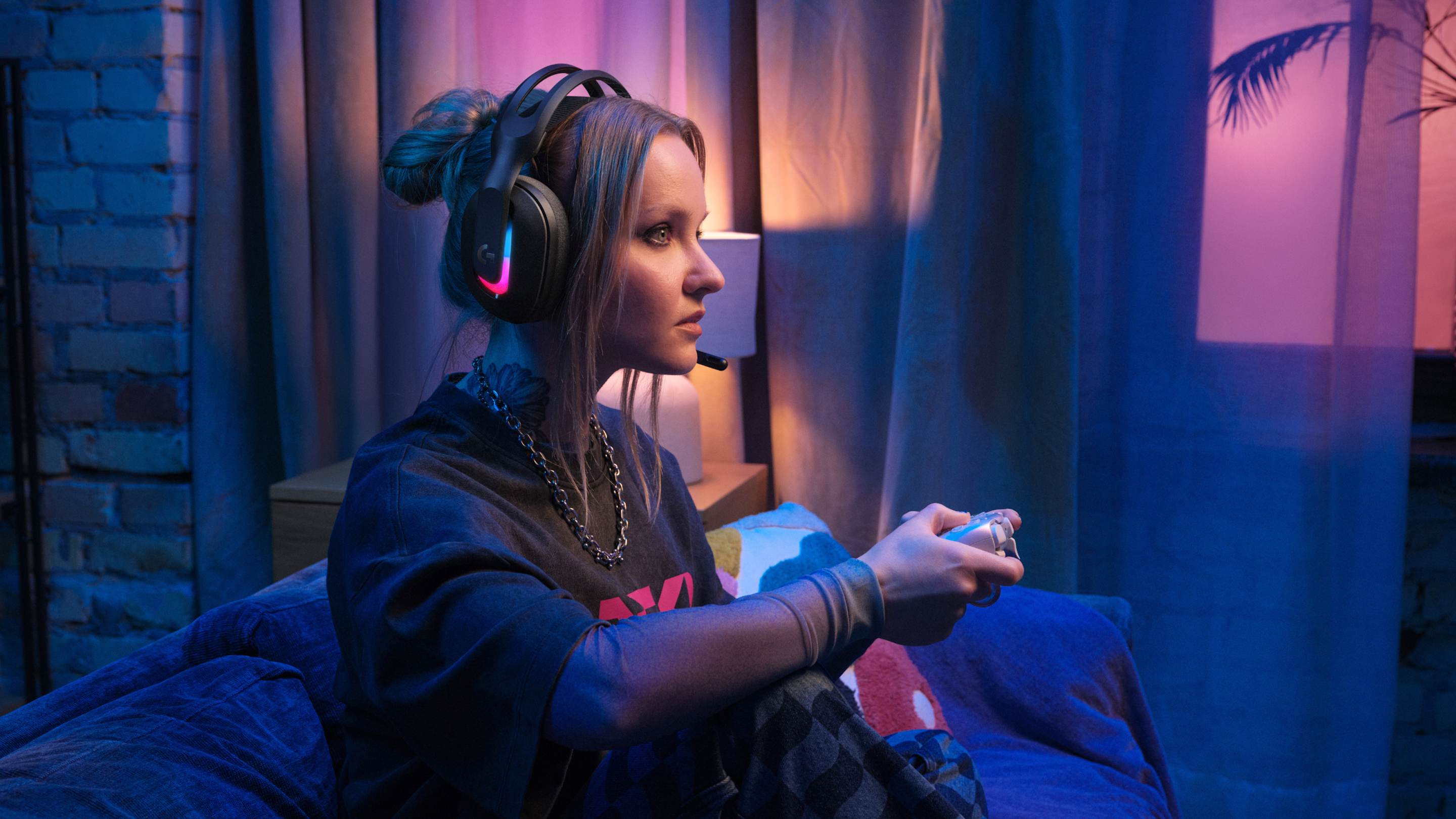 A woman sitting on her couch with a controller in hand, wearing a Logitech Astro A20 X headset.