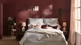 A cream bed in a burgundy bedroom with peach curtains