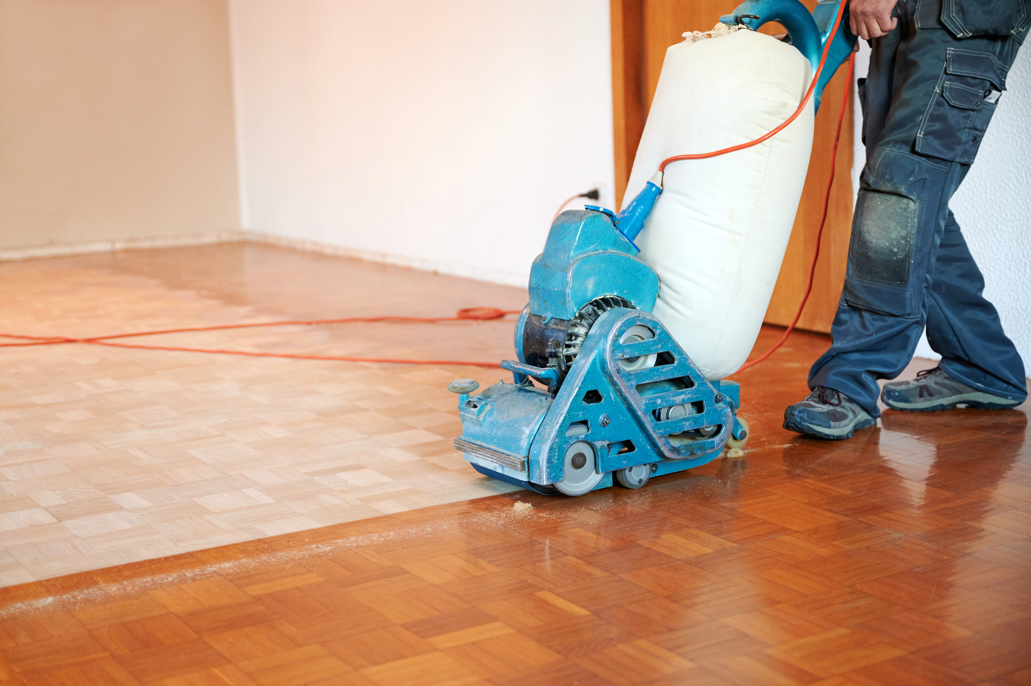 A person pushing a professional-standard floor sander tool across a parquet floor.