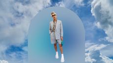 Tan France in a grey suit with shorts and sunglasses on a sky blue background