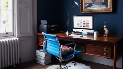 Dark blue home office with dark wooden desk and bright blue office chair