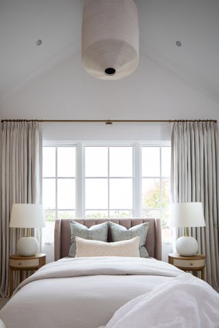 bedrom with white walls and white bed, tall windows with curtains