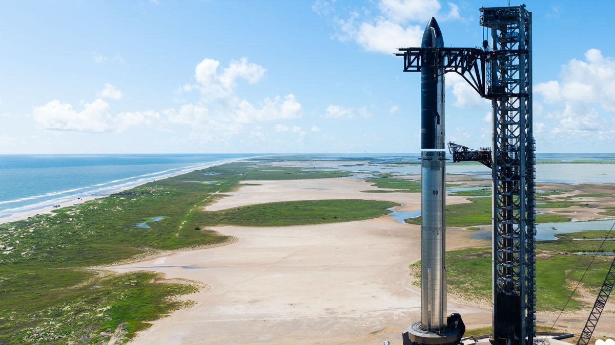 a huge silver rocket stands on a seaside launch pad