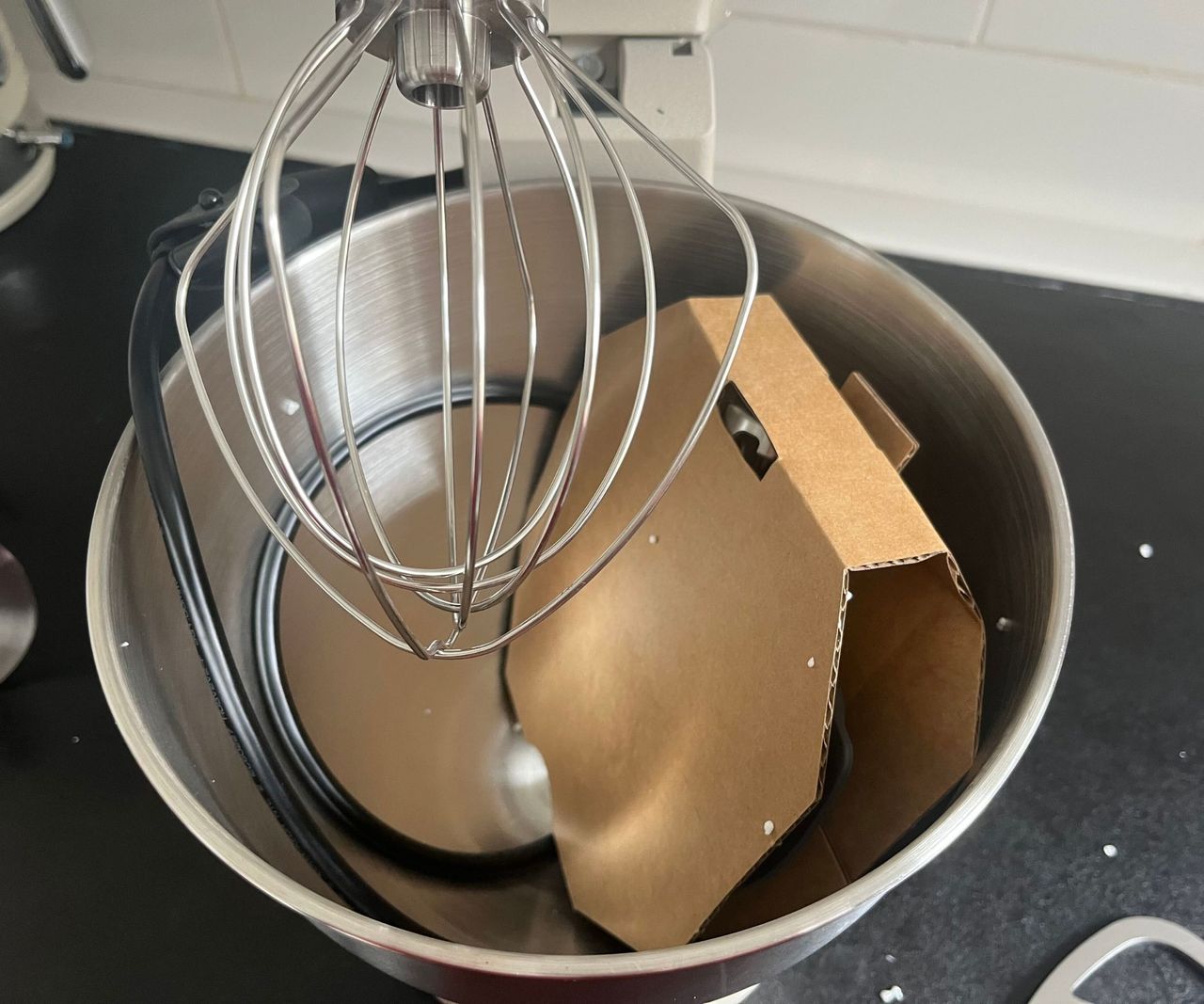 The inside of the newly unboxed KitchenAid Artisan Plus Stand Mixer with the wire whisk attached an the paddle in cardboard packaging inside