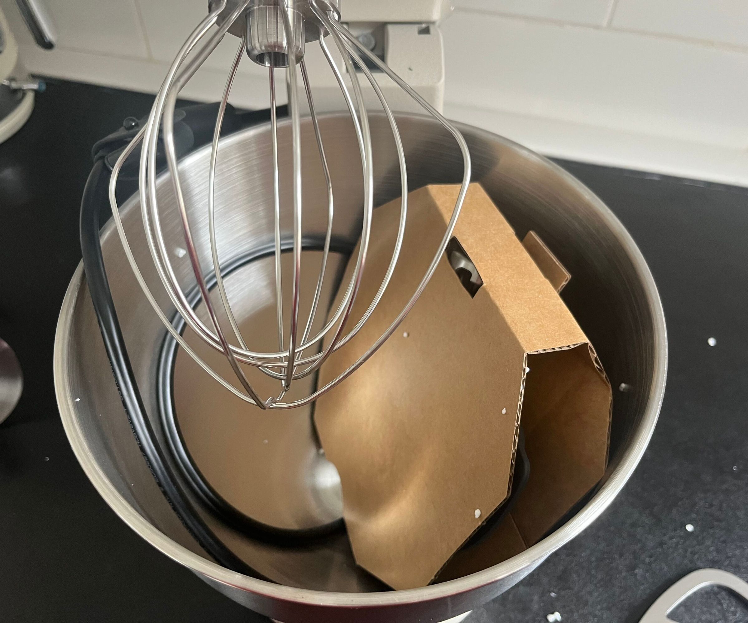 The inside of the newly unboxed KitchenAid Artisan Plus Stand Mixer with the wire whisk attached an the paddle in cardboard packaging inside