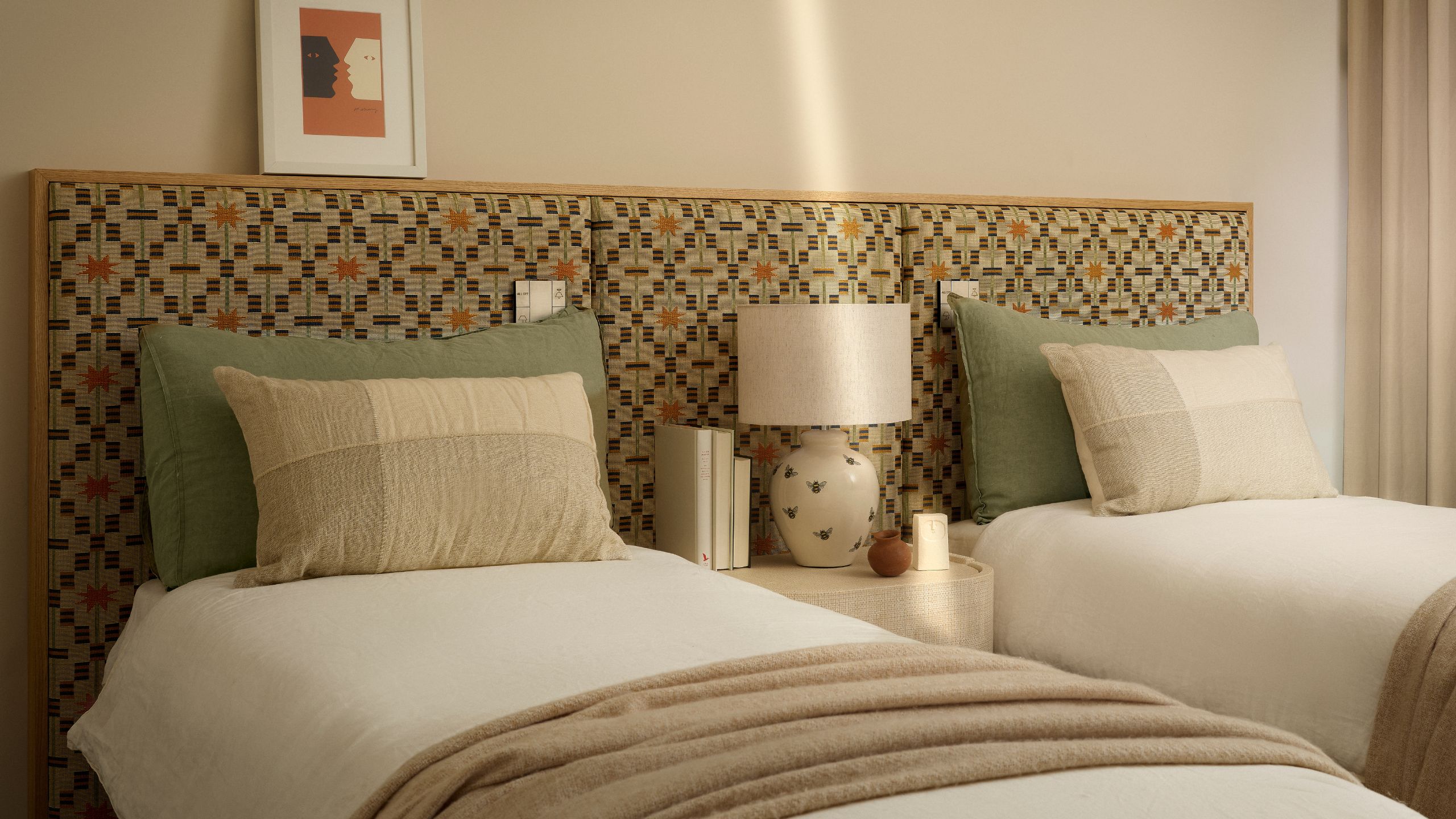 Twin bedroom with patterned headboard, sage pillows, and white bedding with neutral walls.