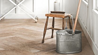 Mop bucket and wooden stool sitting in a white room on wooden flooring