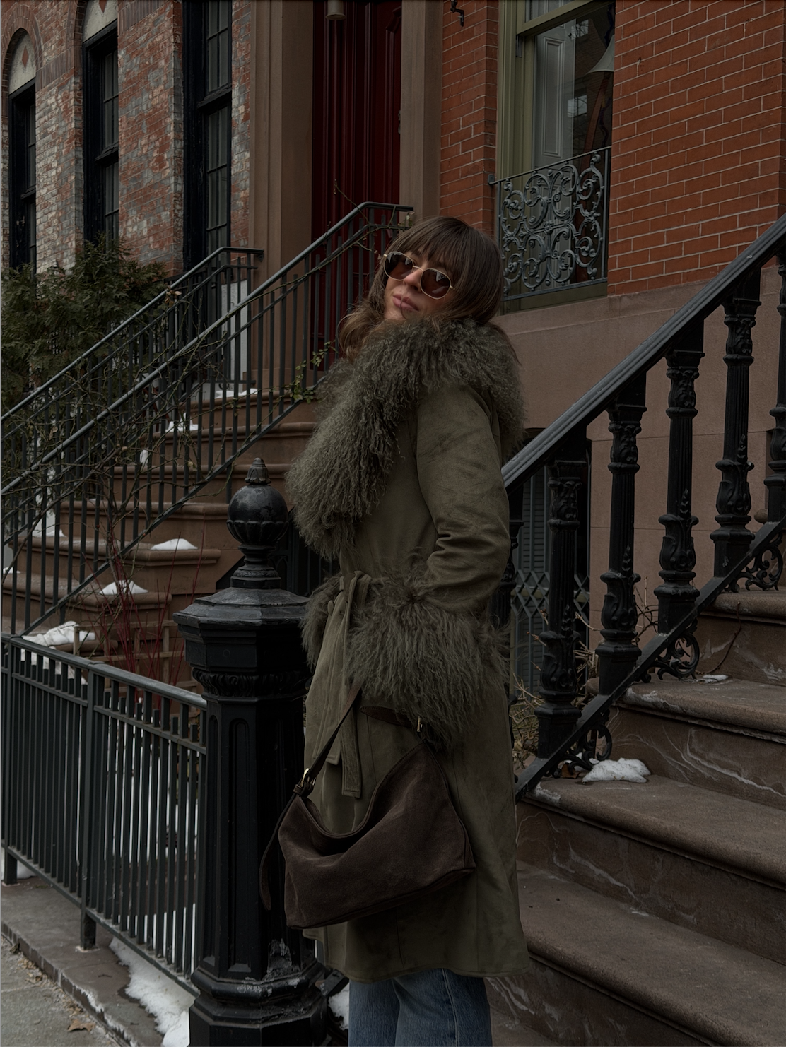 Kathryn Zahorak wearing fur-trimmed green coat, suede bag, jeans, sunglasses in new york city 