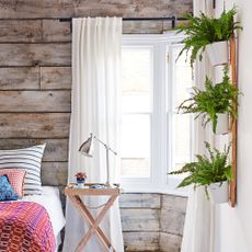 Wood panelled bedroom with sheer curtains, wooden bedside table and plants hanging from wall