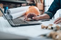 A builder using a computer with plans in the background