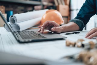 A builder using a computer with plans in the background