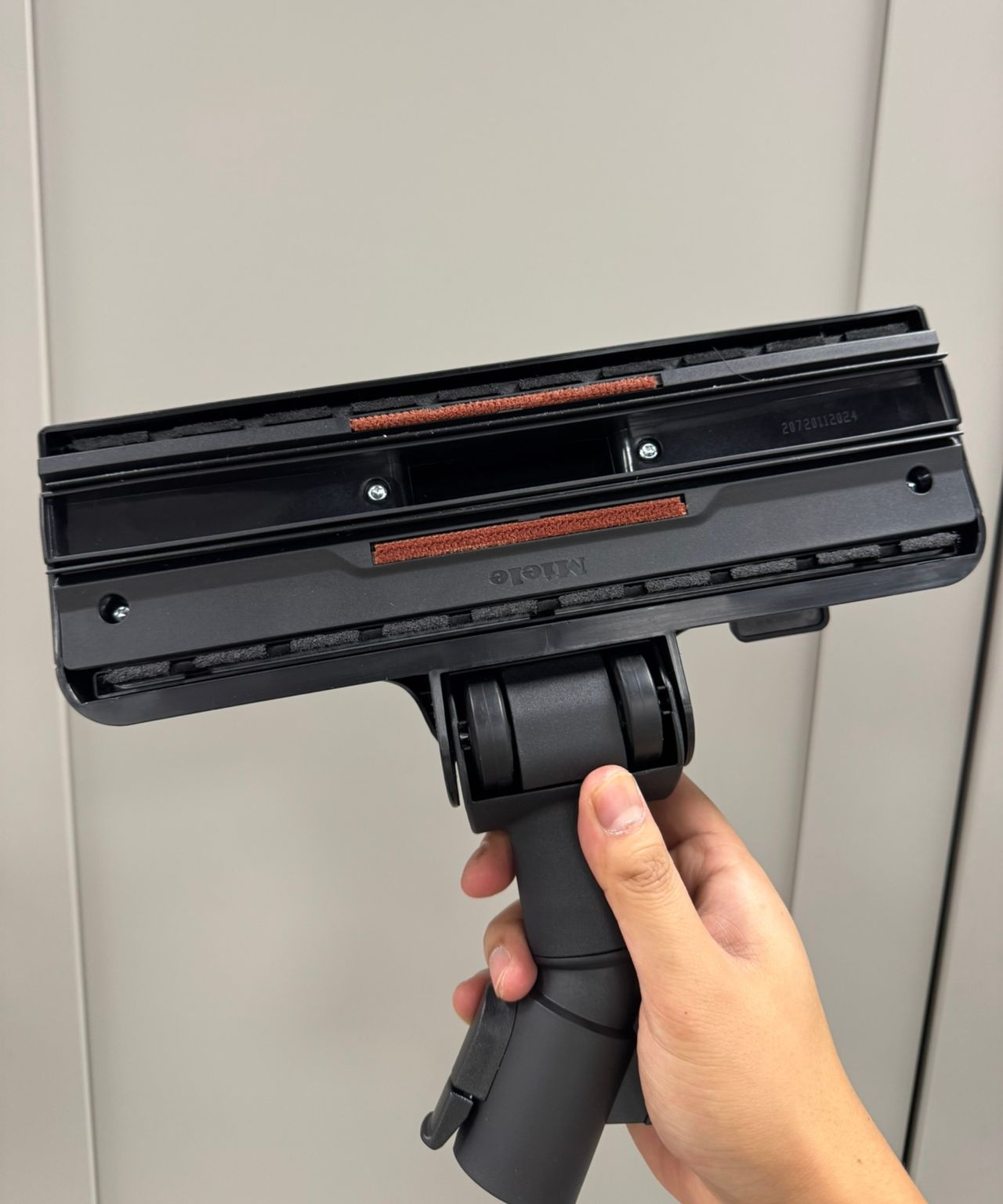 Hand holding the Miele Guard L1 Cat and Dog canister vacuum's universal floorhead in front of gray cabinets.