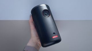 The Nebula Capsule 3 projector is being held to the light against a light grey background.