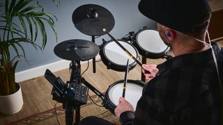 Man wearing a black baseball hat plays a compact electronic drum set