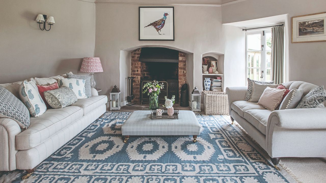 A beige-painted living room with two cream sofas facing each other and an ottoman for a coffee table in the middle