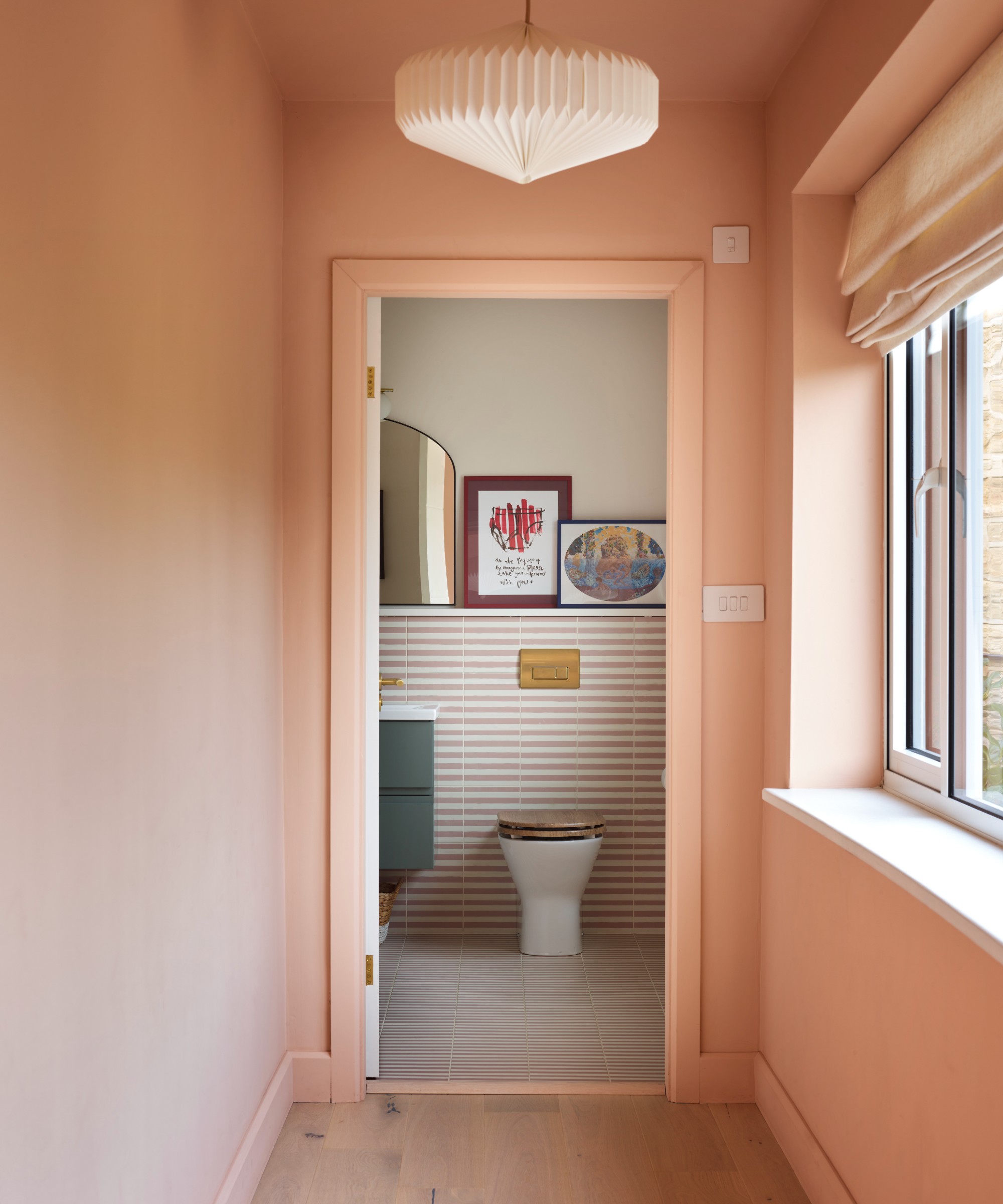 A matt pink-painted colour-drenched hallway with an origami-style pendant light and a view into the bathroom