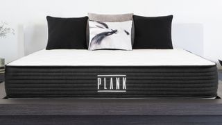 Best firm mattress: the Plank Firm mattress with a black base and white cover, dressed with white, grey and black cushions