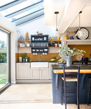 Bright, naturally lit kitchen with dark blue plate rack and island, and exposed brick backsplash idea.