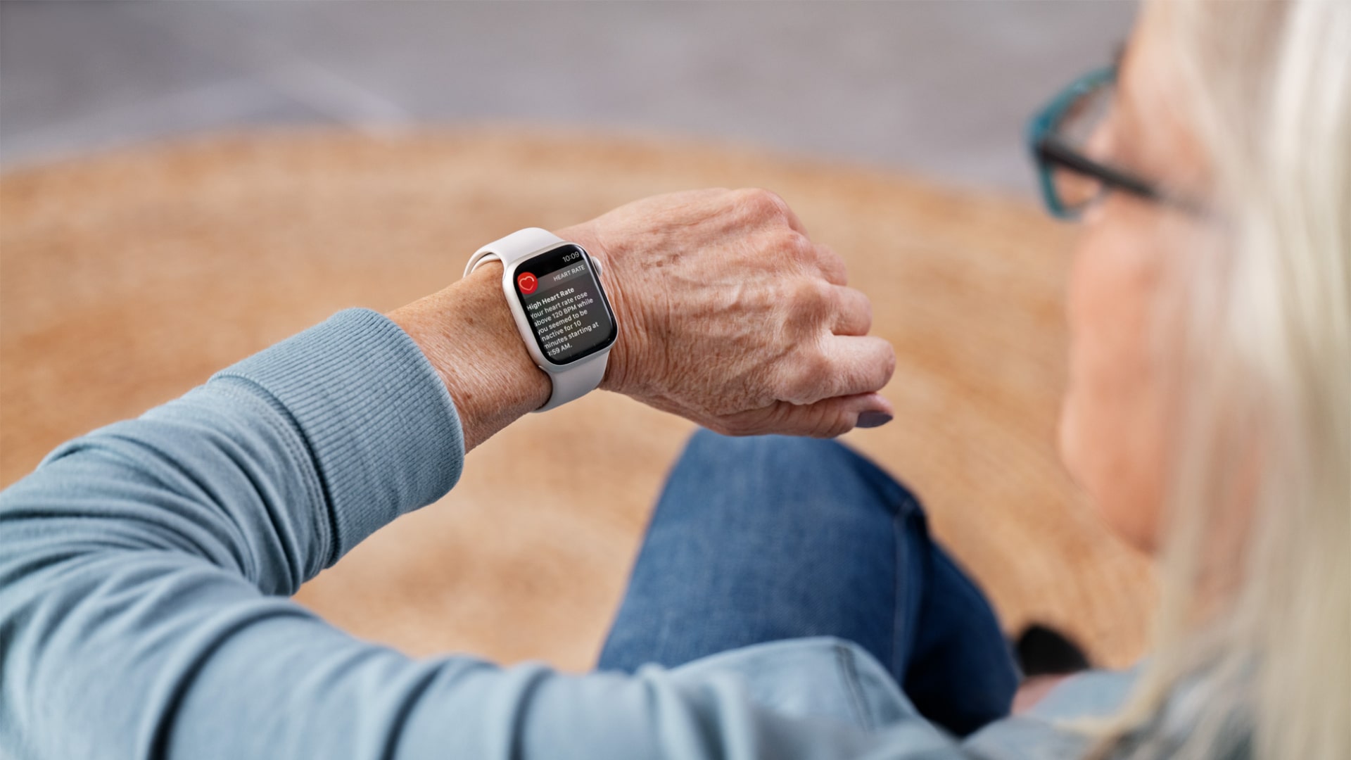 A person looks at an Apple Watch on their wrist. The device is warning them that they have a high heart rate.