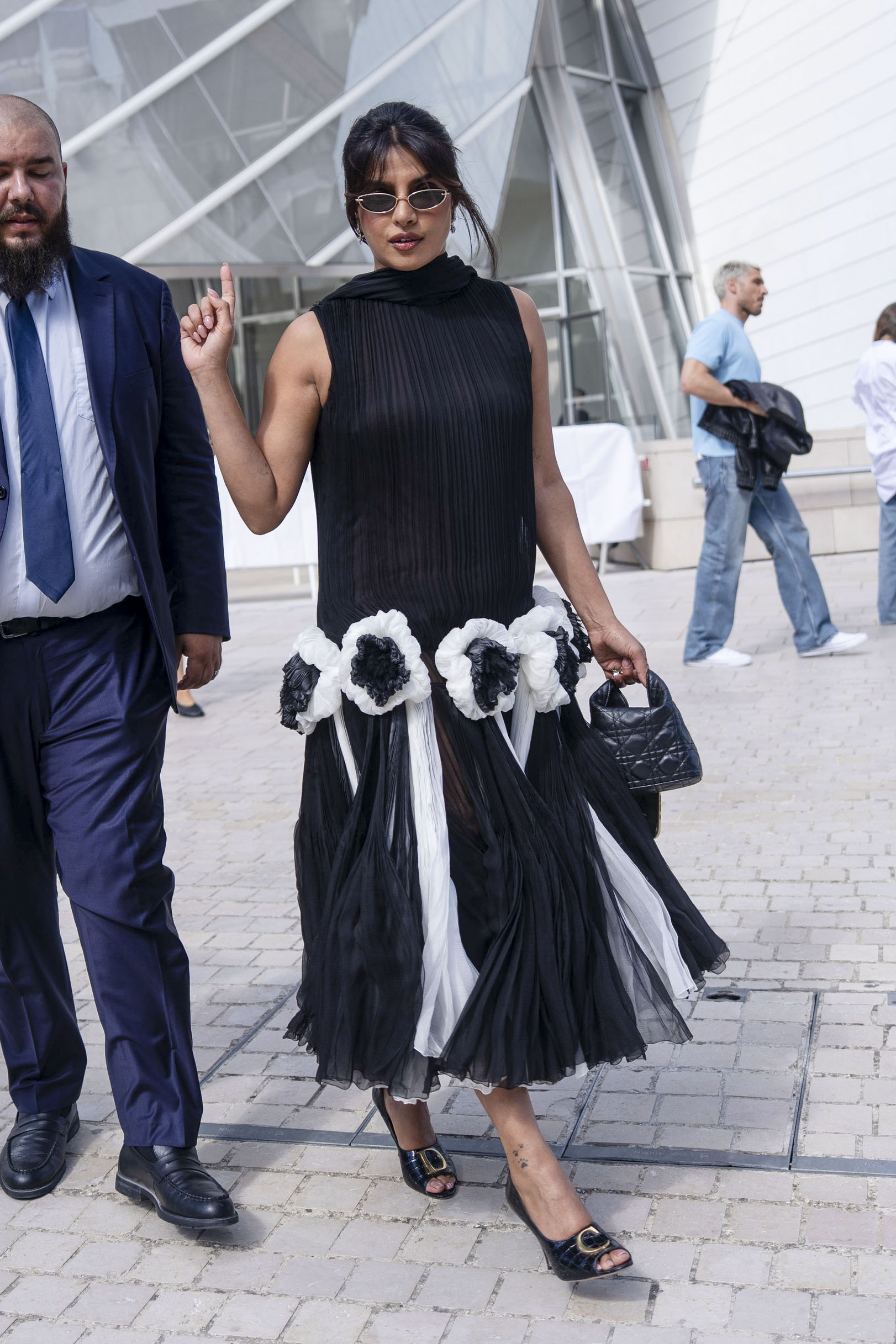 Jennifer Lawrence has long blonde hair and is wearing a black Dior suit, Priyanka Chopra wears her black hair tied back and wears a black Dior dress with a white tiered skirt
