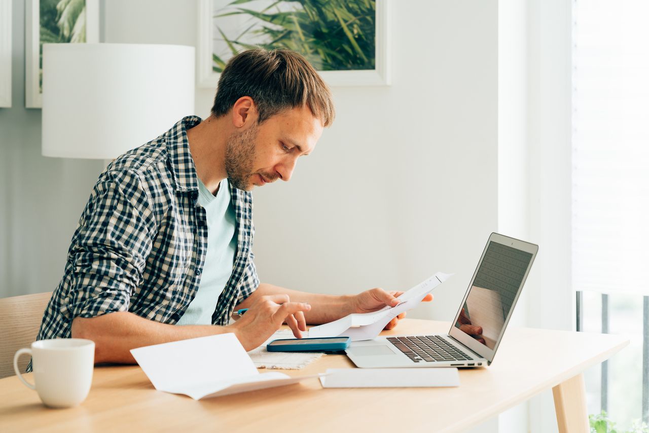 Man using calculator and laptop computer to calculate numbers, perhaps completing a tax return