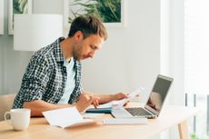 Man using calculator and laptop computer to calculate numbers, perhaps completing a tax return