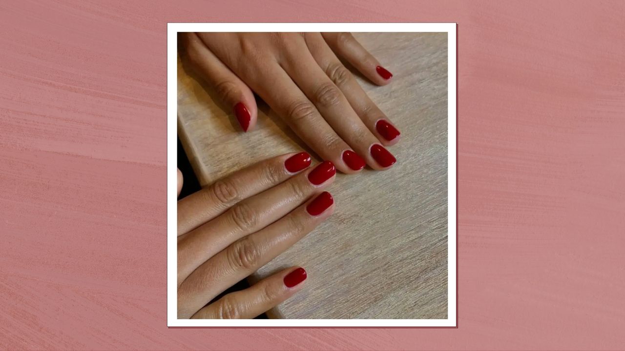 A close-up of two hands with short, red &#039;cranberry&#039;-style nails by nail artist @gel.bymegan/ in a dark pink template