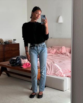 L.A. woman takes a mirror selfie in a The Row sweater, vintage skinny jeans, a black belt and black flats.