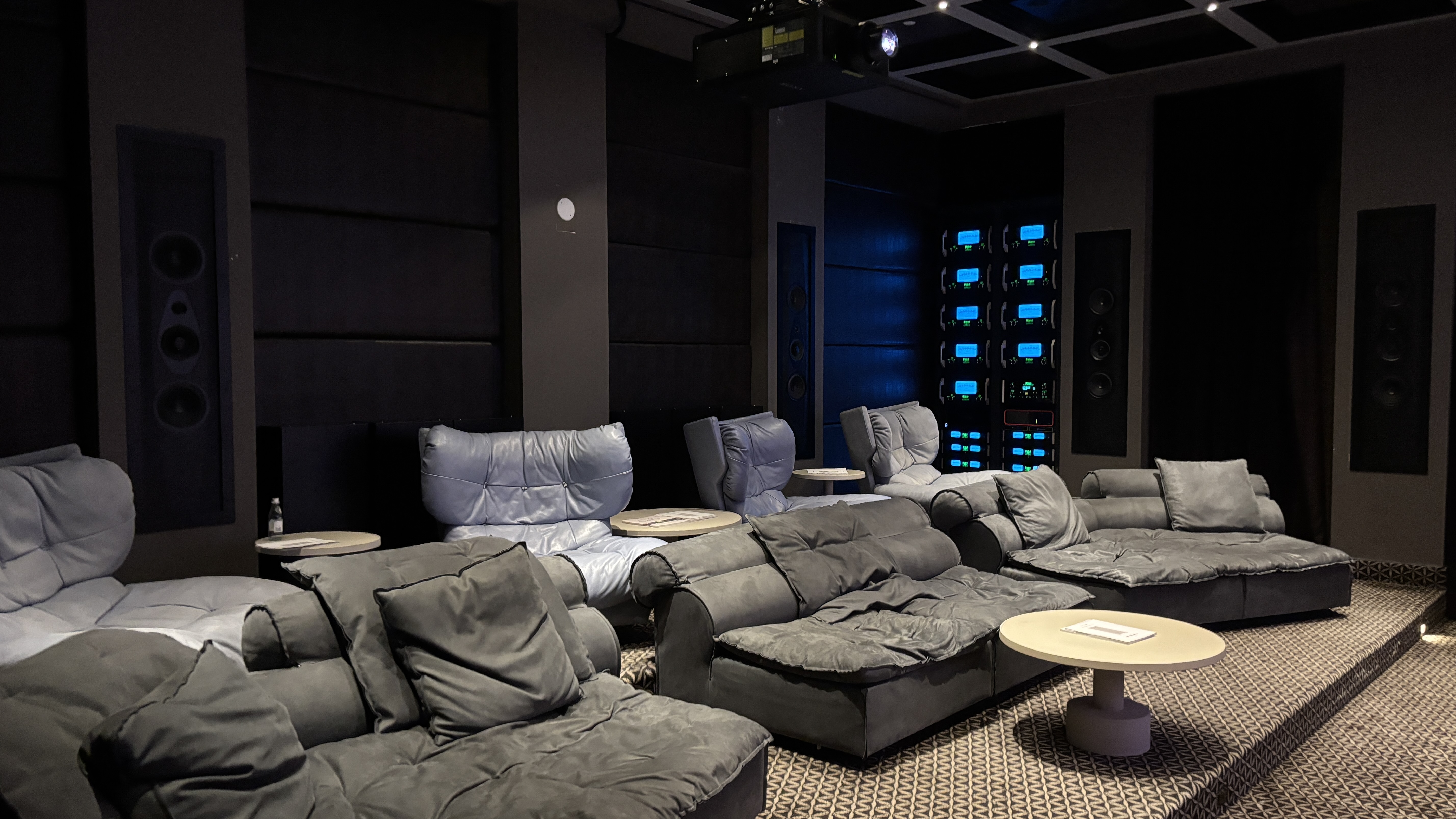The rear of a home cinema room with chairs and and a stack of electronics in the corner with blue backlighting