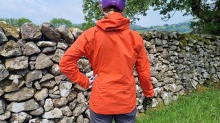 Rear view of woman wearing cycling jacket in front of stone wall in field