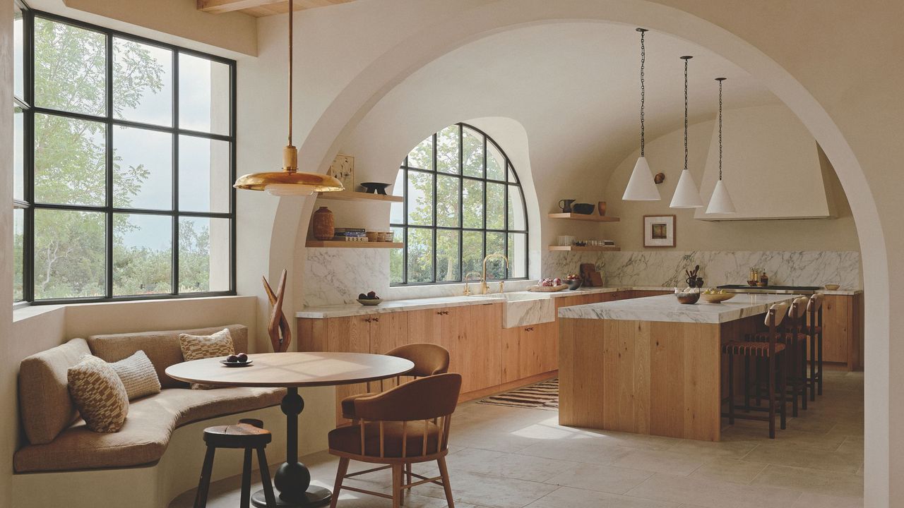 Neutral kitchen with wooden cabinets and marble countertop. The main kitchen is through an arch and there is an arched window to mirror this