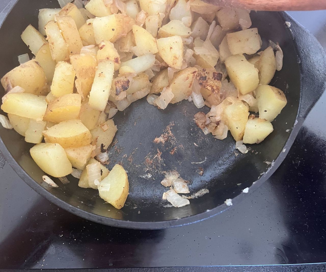 Potatoes and onions frying in a small cast iron pan.
