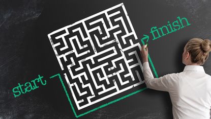 A woman draws a line around a maze on a chalkboard rather than navigating the maze.