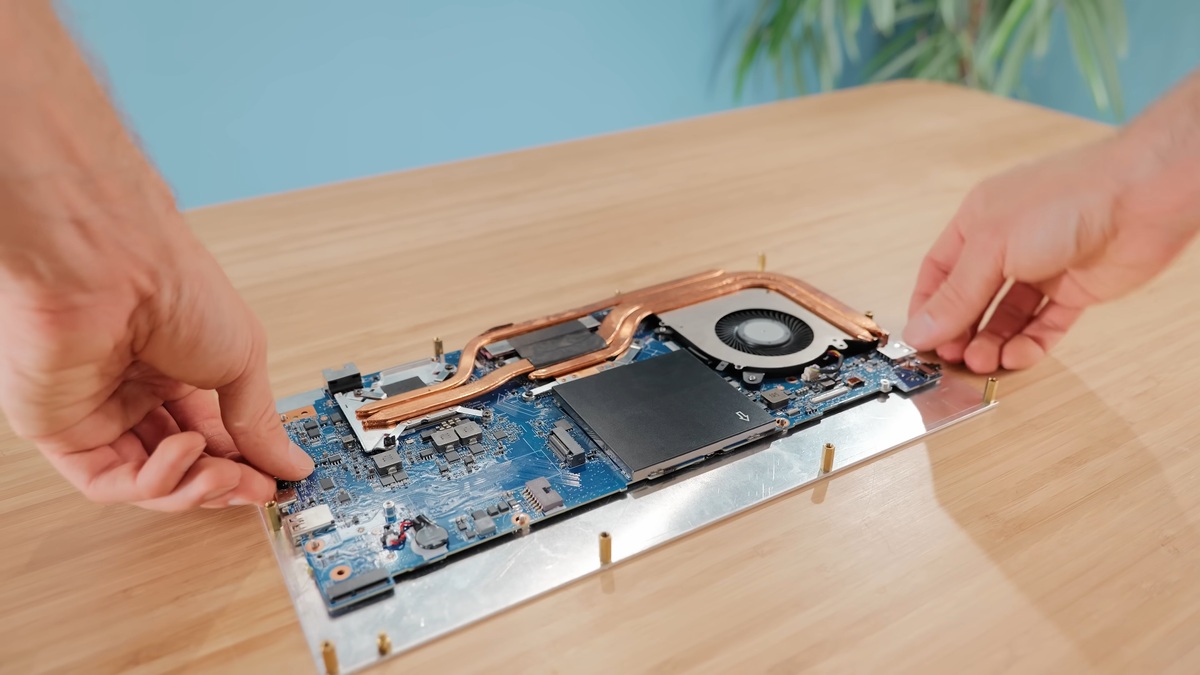 Hands lowering RTX 4060 laptop motherboard into custom aluminium shell.