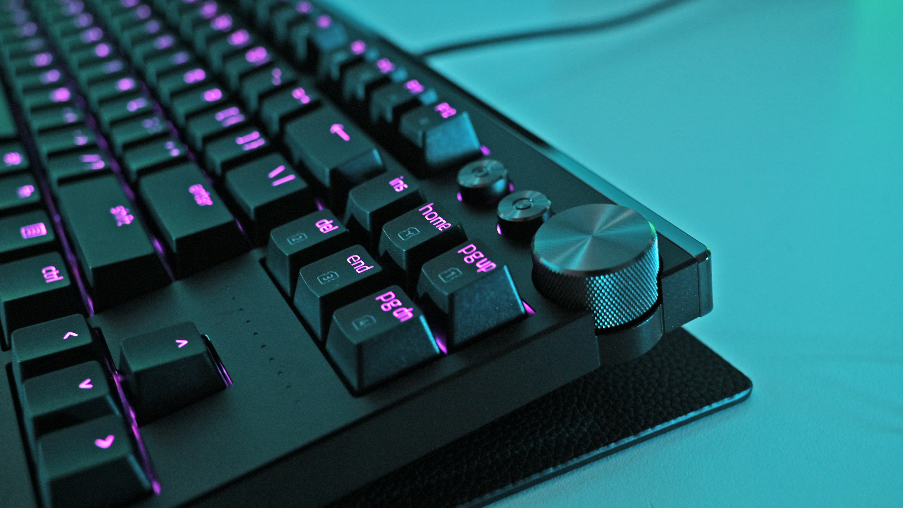 Close-up angled view of the keyboard’s top-right corner, highlighting pink-backlit navigation keys and a prominent textured metallic volume dial.