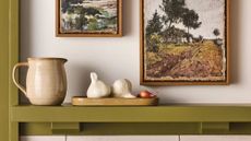 Ceramic objects sitting on a moss green shelf, accented by burlap landscape artwork above