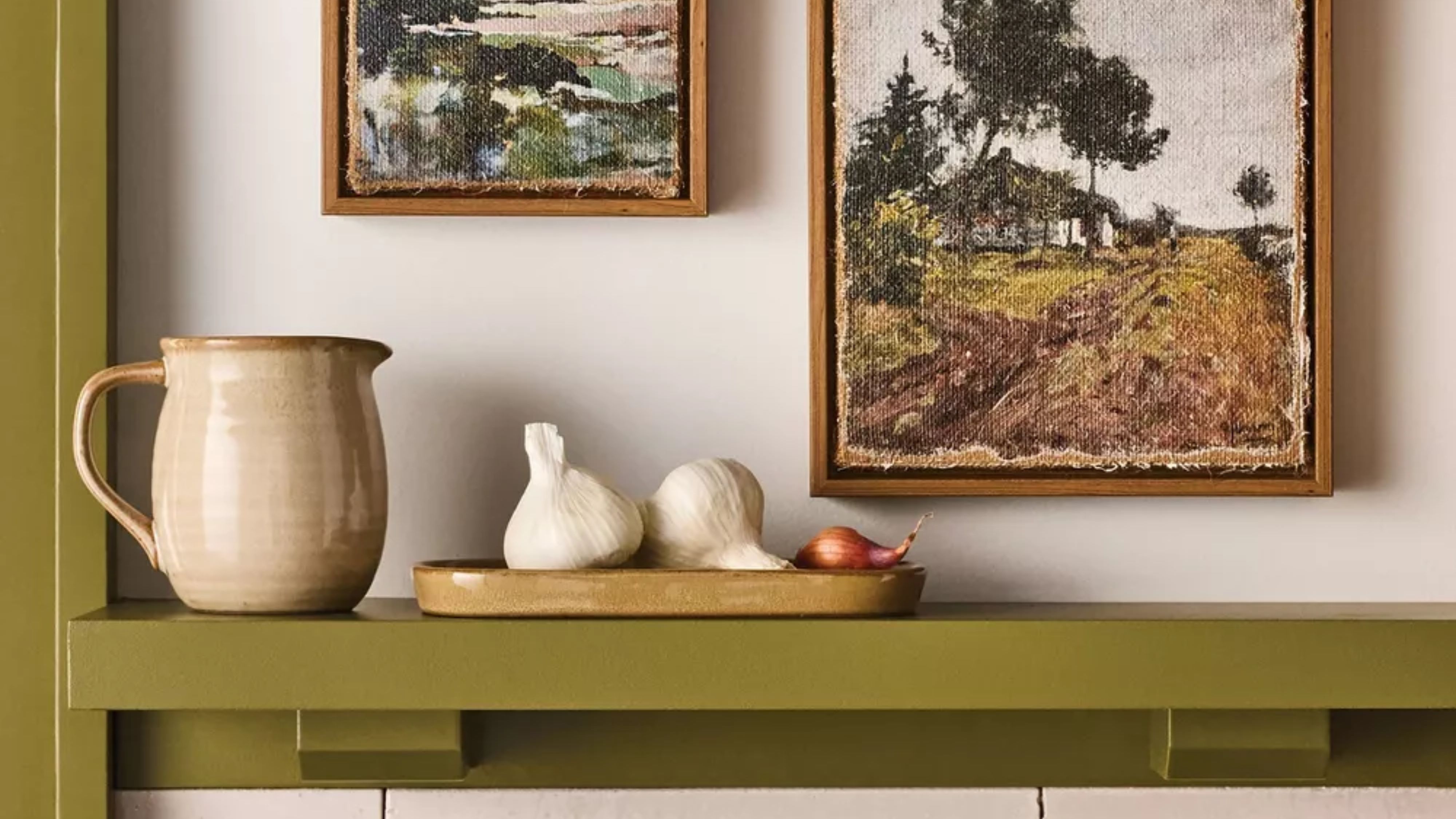 Ceramic objects sitting on a moss green shelf, accented by burlap landscape artwork above