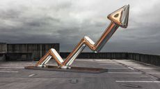 A metallic statue of an arrow pointing up on a parking lot roof.