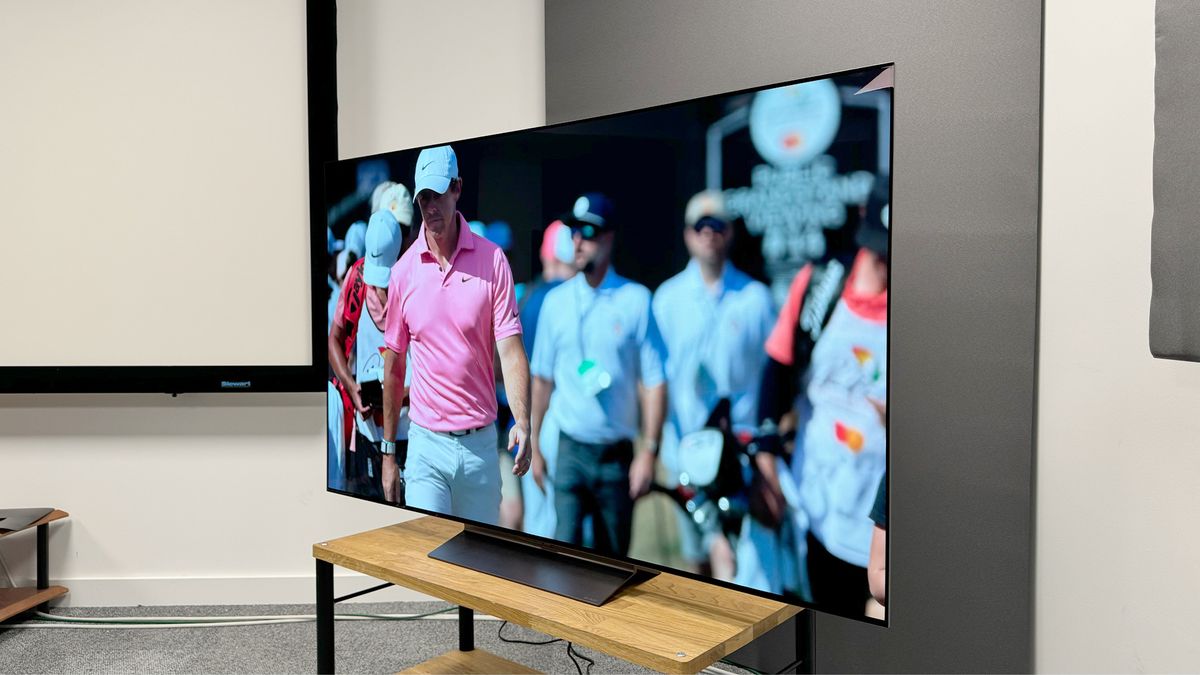 65-inch LG C4 TV photographed at an angle on a wooden stand. On the screen is an image of a golfer in a pink polo shirt.