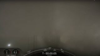 a rocket sits on a launch pad, almost entirely obscured by fog