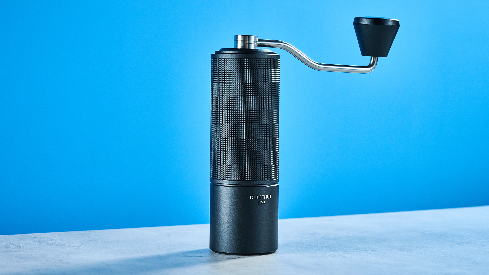 the timemore chestnut c2s coffee grinder in black showing its hand crank and catch chamber photographed against the blue tom's guide background